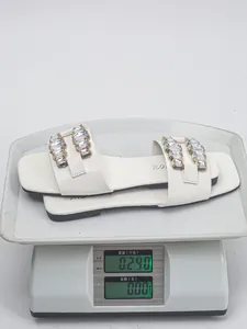 Gros plan de sandales plates blanches avec boucles en cristal sur une balance