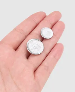 Macro detail of two silver-colored metal buttons with embossed coin design on human hand