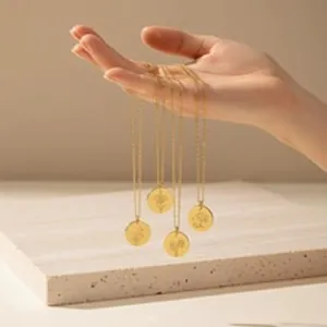 Detailed view of four gold stainless steel floral engraved necklaces held by a hand.