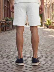 Rear view of men's white waffle-knit casual shorts in an outdoor street setting