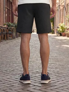 Detailed back view of men's casual dark grey waffle knit shorts on an outdoor street