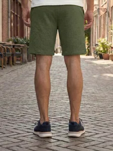 Rear view detail of men's olive green waffle knit casual shorts in a sunlit outdoor street