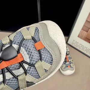 Macro detail of grey breathable mesh fabric on kids' outdoor sneakers with green straps.
