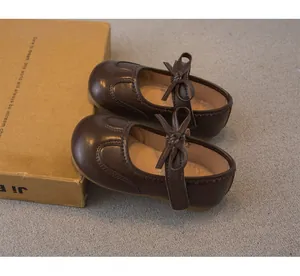 Gros plan de chaussures Mary Jane en cuir marron pour fille avec nœud et bord festonné.