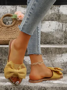 Elegantes sandalias planas amarillas con lazo grande y ribete metálico en escalones de cemento