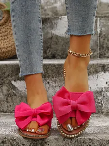 Primer plano de sandalias fucsia con lazo de tela y detalle de tachuelas.