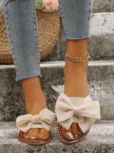 Primer plano de sandalias planas beige con un gran lazo de tela sobre fondo de piedra.
