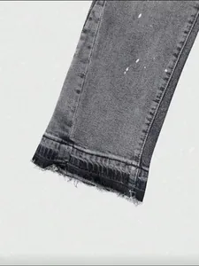 Close-up detail of distressed raw hem and paint splatter on grey washed denim jeans cuff.