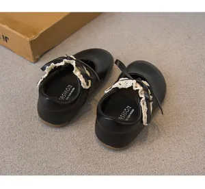 Nahaufnahme schwarzer Prinzessinnenschuhe für Kleinkinder mit cremefarbener Spitze und Schleife
