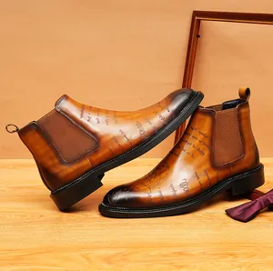 Close-up detail of vintage brown leather Chelsea boots with artistic script patterns.