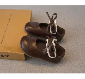 Detailaufnahme von braunen Mädchen-Mary-Janes mit Spitzen-Schleife auf grauem Grund