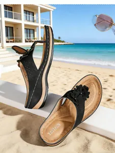 Détail de sandales noires à plateforme avec fleurs sur une plage tropicale