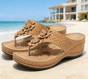 Vue détaillée de sandales compensées marron avec fleurs sur une plage ensoleillée.