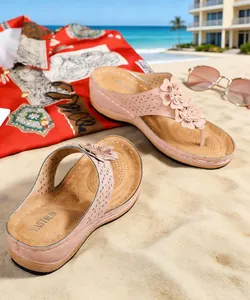 Vue détaillée des sandales compensées roses avec fleurs sur une plage ensoleillée.