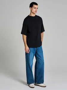 Full-body studio shot of a man wearing a black oversized heavy cotton t-shirt and wide-leg jeans.