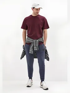 Full body view of a stylish man wearing a maroon t-shirt and navy athletic joggers.