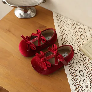 Zapatos Mary Jane de terciopelo rojo para bebé con lazos sobre una mesa rústica de madera