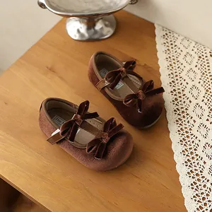 Vista detallada de zapatos para bebé en terciopelo marrón con lazos dobles y cierre de hebilla