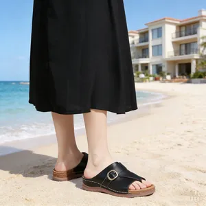 Detailed view of black stitched sandals with metal buckle on a sunny sandy beach background