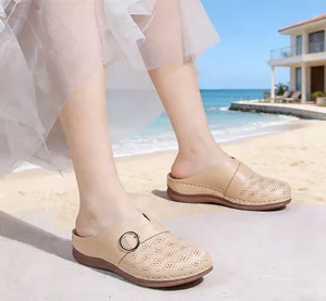 Side view of beige closed-toe mules on a sandy beach showing buckle and laser-cut texture