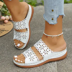 Detail von weißen Damen-Keilsandalen mit durchbrochenem Blumenmuster an den Füßen