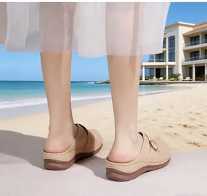 Rear view of women's beige wedge clogs with decorative stitching on a sunny beach