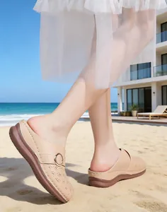 Elegant beige women's closed-toe wedge mules with decorative stitching on a sunny beach