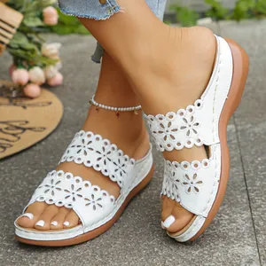 Detailansicht weißer Keilsandalen mit eleganten floralen lasergeschnittenen Mustern.