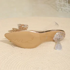 Detailansicht der champagnergoldenen Sandalen mit Strassschleife und klarem Absatz.