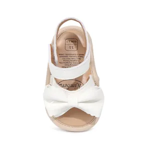 Détail d'une sandale blanche brillante pour bébé avec gros nœud et scratch velcro