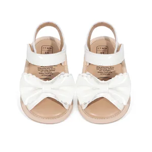 Vue détaillée de sandales en cuir verni blanc pour bébé avec une grande décoration de nœud.