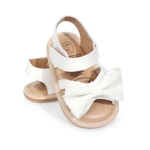 Détail de sandales blanches brillantes pour bébé avec un nœud décoratif et semelle souple