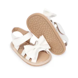 Sandales pour bébé blanches brillantes avec nœud décoratif et semelle en caoutchouc.