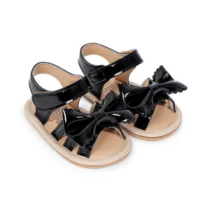 Gros plan de sandales pour bébés en cuir verni noir avec grand nœud et scratch de fermeture