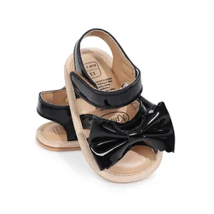 Gros plan de sandales pour bébé en cuir verni noir avec un grand nœud décoratif chic.