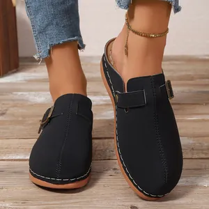 Detail view of women's black closed-toe mules with buckle decoration and white stitching