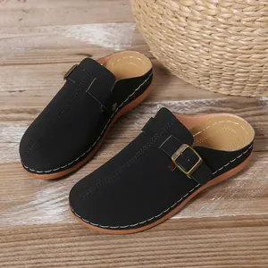 Detail view of black women's wedge clogs with gold buckle and white stitching