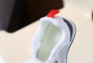 Close-up of soft mesh inner lining and red pull tab on white baby toddler shoes.