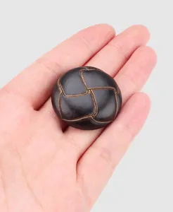 Gros plan d'un bouton décoratif en nylon tressé noir tenu dans la main pour l'échelle