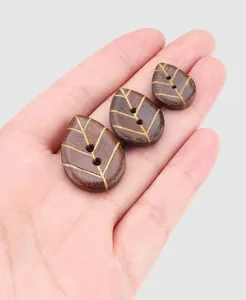Detailed view of hand-held leaf-shaped ebony wood buttons with intricate vein patterns.