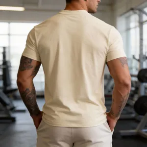 Back view of a men's athletic crew neck T-shirt in cream color within a gym setting