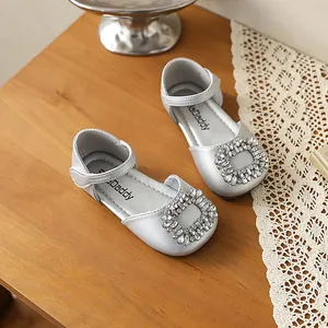 Detailed view of silver girl's princess shoes with a luxury rhinestone buckle on wooden table