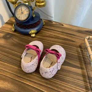 Detailed macro view of pink glitter baby princess shoes with magenta bows on a wooden table