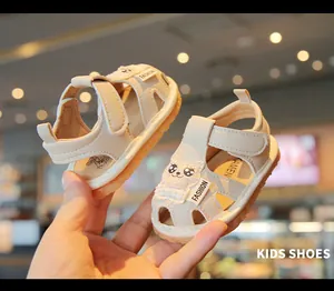Close-up of beige infant walking sandals with cute cartoon cat patch and soft sole