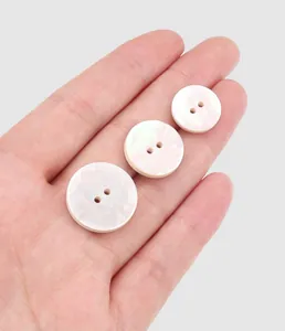 Detailed view of three iridescent white mother of pearl buttons in different sizes on a palm.