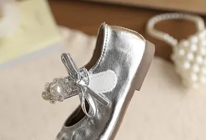 Detail van een zilveren prinsessenschoen voor meisjes met parelband en strikje