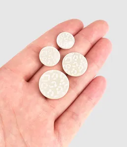 Détail de boutons en nacre blanche avec motif léopard dans la main pour l'échelle.
