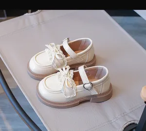 Detailansicht von cremefarbenen Mädchen-Mary Janes mit Spitzenschleife und Herzschnalle.