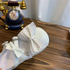 Detalle en primer plano de zapatos Lolita blancos con lazos de lunares rosas y encaje.