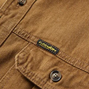 Détail rapproché de la poche et de l'étiquette sur une chemise en jean marron